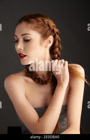 Modèle féminin élégant avec cheveux rouges et tresses studio sur fond sombre et vue sur l'extérieur Banque D'Images