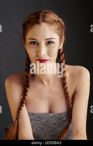 Modèle féminin élégant avec cheveux rouges et tresses studio sur fond sombre et regardant l'appareil photo Banque D'Images