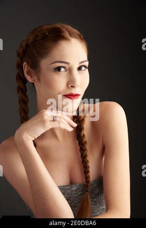 Modèle féminin élégant avec cheveux rouges et tresses studio sur fond sombre et regardant l'appareil photo Banque D'Images