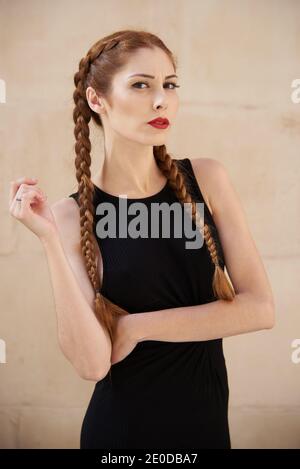 Modèle féminin élégant avec cheveux rouges et tresses studio sur fond sombre et regardant l'appareil photo Banque D'Images