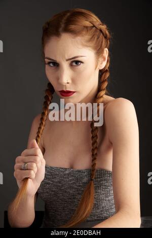 Modèle féminin élégant avec cheveux rouges et tresses studio sur fond sombre et regardant l'appareil photo Banque D'Images