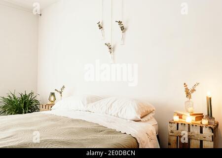 Chambre lumineuse avec intérieur minimaliste, lit confortable et bois mobilier avec décoration boho sur mur blanc Banque D'Images