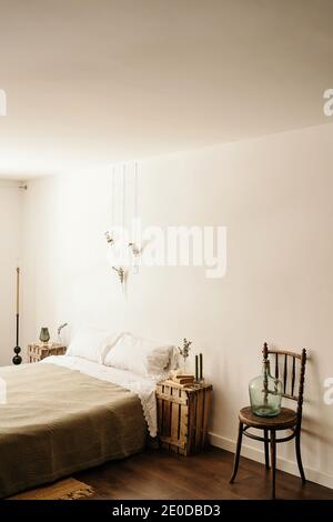 Chambre lumineuse avec intérieur minimaliste, lit confortable et bois mobilier avec décoration boho sur mur blanc Banque D'Images