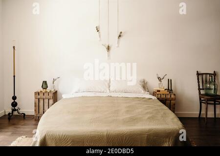 Chambre lumineuse avec intérieur minimaliste, lit confortable et bois mobilier avec décoration boho sur mur blanc Banque D'Images