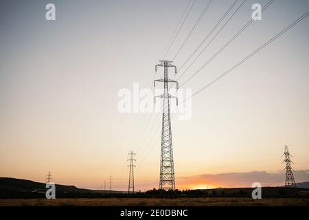 Faible angle des grandes tours électriques et des câbles sur le terrain sous le ciel du soir, le soleil se couche sur la ligne d'horizon l'été Banque D'Images