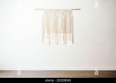 Décoration en coton macrame de style boho écologique sur bâton de bois suspendu au mur blanc dans une salle lumineuse à l'intérieur minimaliste Banque D'Images