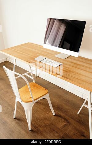 Ordinateur moderne placé sur une table en bois près d'une chaise dans un cadre contemporain chambre lumineuse avec intérieur minimaliste Banque D'Images