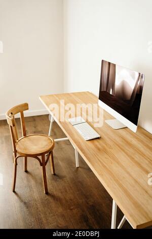 Ordinateur moderne placé sur une table en bois près d'une chaise dans un cadre contemporain chambre lumineuse avec intérieur minimaliste Banque D'Images