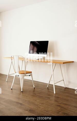 Ordinateur moderne placé sur une table en bois près d'une chaise dans un cadre contemporain chambre lumineuse avec intérieur minimaliste Banque D'Images