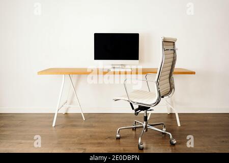 Ordinateur moderne placé sur une table en bois près d'une chaise dans un cadre contemporain chambre lumineuse avec intérieur minimaliste Banque D'Images