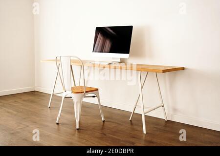 Ordinateur moderne placé sur une table en bois près d'une chaise dans un cadre contemporain chambre lumineuse avec intérieur minimaliste Banque D'Images