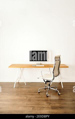 Ordinateur moderne placé sur une table en bois près d'une chaise dans un cadre contemporain chambre lumineuse avec intérieur minimaliste Banque D'Images