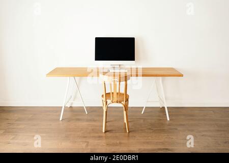 Ordinateur moderne placé sur une table en bois près d'une chaise dans un cadre contemporain chambre lumineuse avec intérieur minimaliste Banque D'Images