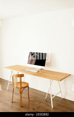 Ordinateur moderne placé sur une table en bois près d'une chaise dans un cadre contemporain chambre lumineuse avec intérieur minimaliste Banque D'Images