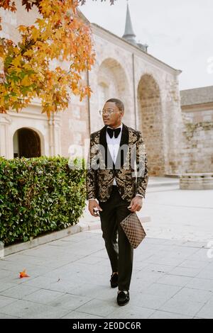 Élégant Afro-américain mâle portant un tuxedo cher marchant le long de la rue et regarder loin Banque D'Images