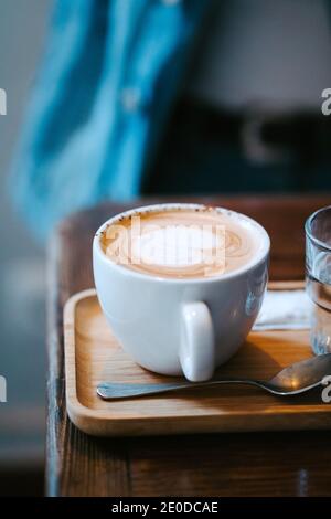 Tasse en céramique blanche avec cappuccino frais et aromatique chaud au cœur latte en forme d'art servie avec une cuillère sur un plateau en bois tableau Banque D'Images