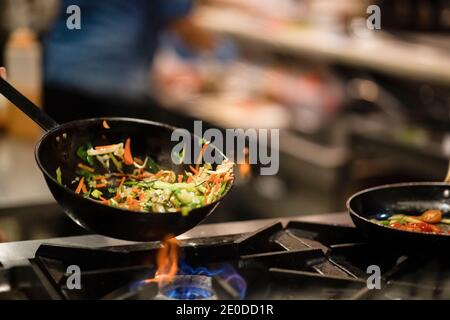 Poêle à frire avec légumes frits remués par un cuisinier anonyme pendant la préparation sur cuisinière à gaz dans la cuisine du restaurant Banque D'Images