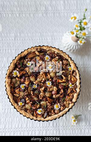Vue de dessus de tarte sucrée avec diverses baies séchées servi sur table avec bouquet de fleurs de camomille dans le rustique cuisine Banque D'Images
