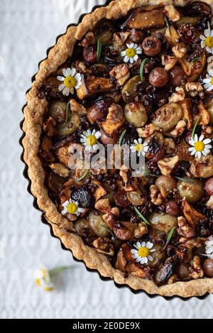 Vue de dessus de tarte sucrée avec diverses baies séchées servi sur table avec bouquet de fleurs de camomille dans le rustique cuisine Banque D'Images