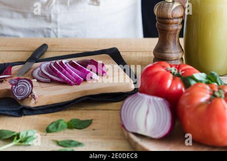 Tranches d'oignon frais sur planche à découper en bois avec ingrédients pour la soupe de tomates dans la cuisine Banque D'Images