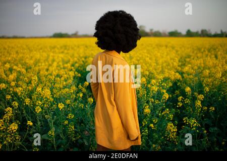 Vue arrière de jeunes Afro-américaines méconnaissables avec du murali cheveux vêtus de vêtements noirs et jaunes tout en étant debout au milieu flux jaune vif Banque D'Images