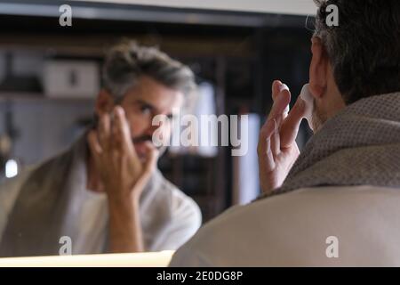 Photo de l'homme d'âge moyen avec des cheveux gris se préparant à raser sa barbe dans la salle de bains. Banque D'Images