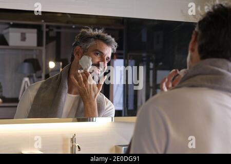 Photo de l'homme d'âge moyen avec des cheveux gris se préparant à raser sa barbe dans la salle de bains. Banque D'Images