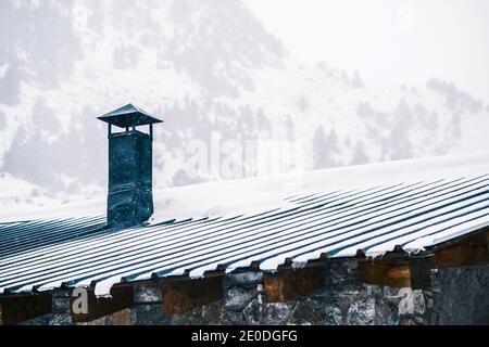 Cheminée sur le toit d'une petite maison résidentielle située en montagne campagne couverte de neige le jour d'hiver nuageux Banque D'Images