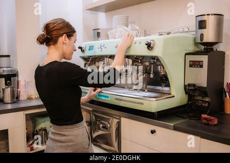 Vue latérale d'une femme de café utilisant une machine à café pendant préparation de la boisson chaude à la commande Banque D'Images
