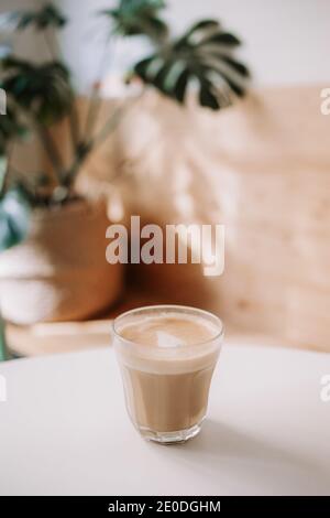 Tasse en verre de café aromatique avec du lait placé sur la table dans un café confortable et léger Banque D'Images