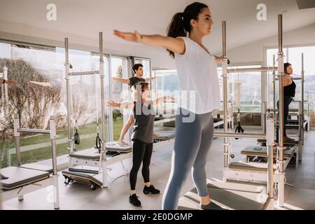 Groupe de personnes en activité debout sur pilates réformateurs dans Cinq étoiles pointues pose et pratiquer le yoga sous la supervision de entraîneur dans la salle de sport moderne Banque D'Images