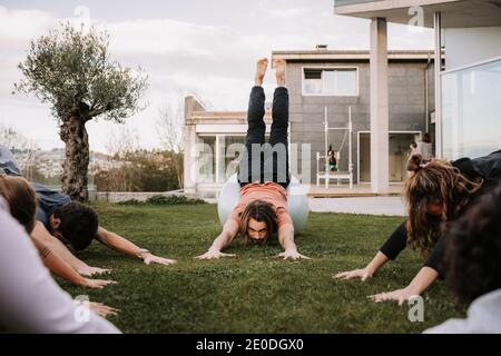 Groupe de personnes dans les vêtements de sport allongé sur les balles et se pencher sur la pelouse tout en faisant de l'entraînement pilates ensemble dans l'arrière-cour Banque D'Images