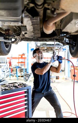 Un technicien homme très occupé utilise un instrument spécial et fixe la voiture pendant travailler dans un service moderne Banque D'Images