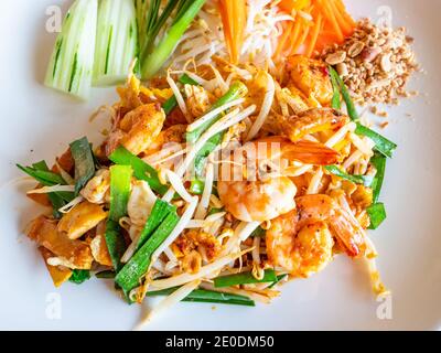 Le plat thaïlandais classique Pad Thai, composé de nouilles frites avec crevettes, pousses de haricots, tofu frit, arachides écrasées et oignon de printemps, avec concombre et an Banque D'Images