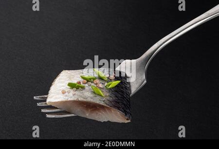 Morceaux de hareng salé sur la fourche sur fond noir Banque D'Images