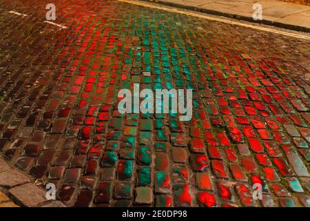 Une route pavée à Leeds avec des reflets des lumières d'une entreprise à proximité. Banque D'Images