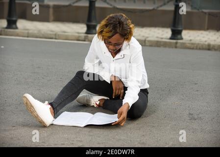 Belle jeune fille concentrée étudiant assis sur le campus de l'université faisant la lecture. Belle fille dans des vêtements décontractés à l'extérieur à l'université. Conc. Étudiant Banque D'Images