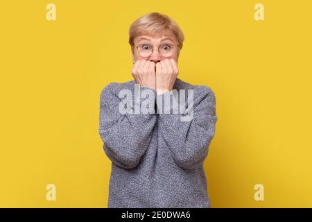 Peur femme inquiète, mordant les ongles. Studio tourné sur un mur jaune. Banque D'Images