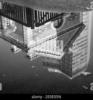 Image monochrome noir et blanc des anciens et des nouveaux bâtiments se reflète dans la flaque d'eau de la route Banque D'Images