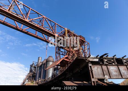 Ancienne aciérie avec trusques suspendues, hauts fourneaux rouillés contre un ciel bleu, aspect horizontal Banque D'Images