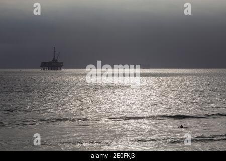 Derrick de pétrole et surfeurs au large de la côte de Huntington Beach, Orange County, Californie, États-Unis Banque D'Images