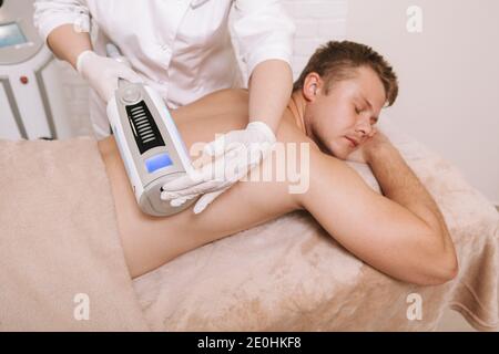 Patient masculin recevant un massage des endosphères à la clinique de beauté. Cosmétologue effectuant un massage arrière d'un client à l'aide d'un périphérique endosphères Banque D'Images