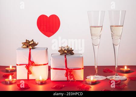 Composition de la Saint-Valentin avec deux verres de champagne, coeur, cadeaux et bougies sur fond rouge. Concept de San Valentin et d'Amour. Banque D'Images