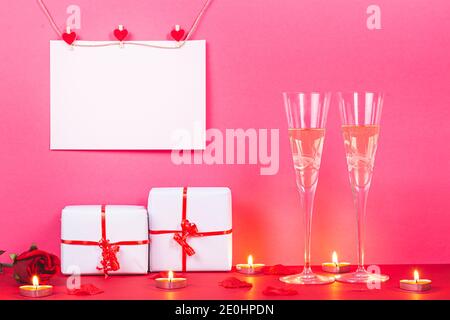 Carte de Saint-Valentin avec coeurs, cadeaux, rose, bougies et deux verres de champagne sur fond rose. Concept de San Valentin et d'Amour. Banque D'Images