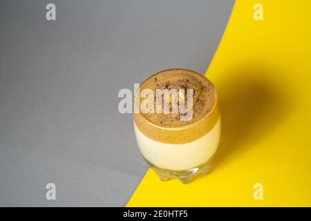 Café Dalgona avec mousse luxuriante dans un verre sur fond jaune et gris. Boisson coréenne tendance Banque D'Images