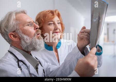 Gros plan d'un médecin barbu senior parlant à son collègue de travail féminin, regardant l'IRM d'un patient Banque D'Images