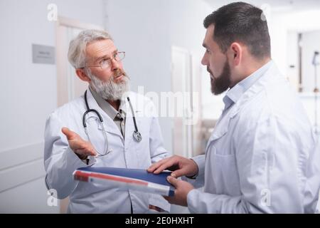 Médecin senior parlant à son jeune stagiaire. Deux médecins de sexe masculin discutant dans le hall d'un hôpital Banque D'Images