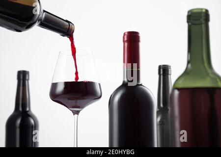 Bouteille de vin rouge versée dans le verre de vin, et variété de bouteilles de vin avec une attention sélective sur fond blanc. Banque D'Images