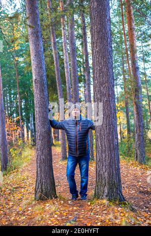 Un homme dans une veste et un chapeau marche à travers la forêt d'automne parmi de grands pins. Passe-temps extérieur. Banque D'Images