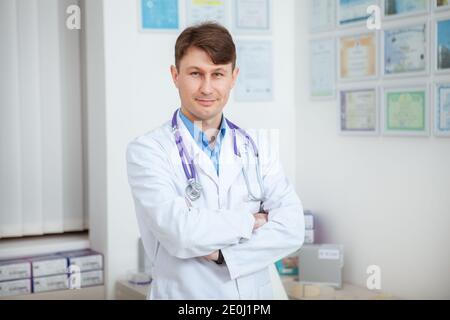 Expérimenté homme médecin confiant souriant à l'appareil photo avec son bras croisés Banque D'Images